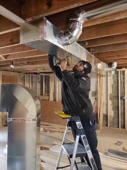 A man on a ladder working on an air duct.