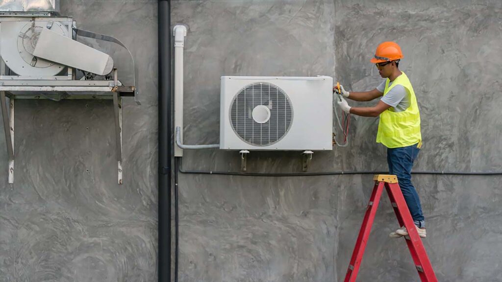 A man on a ladder fixing air conditioning unit.