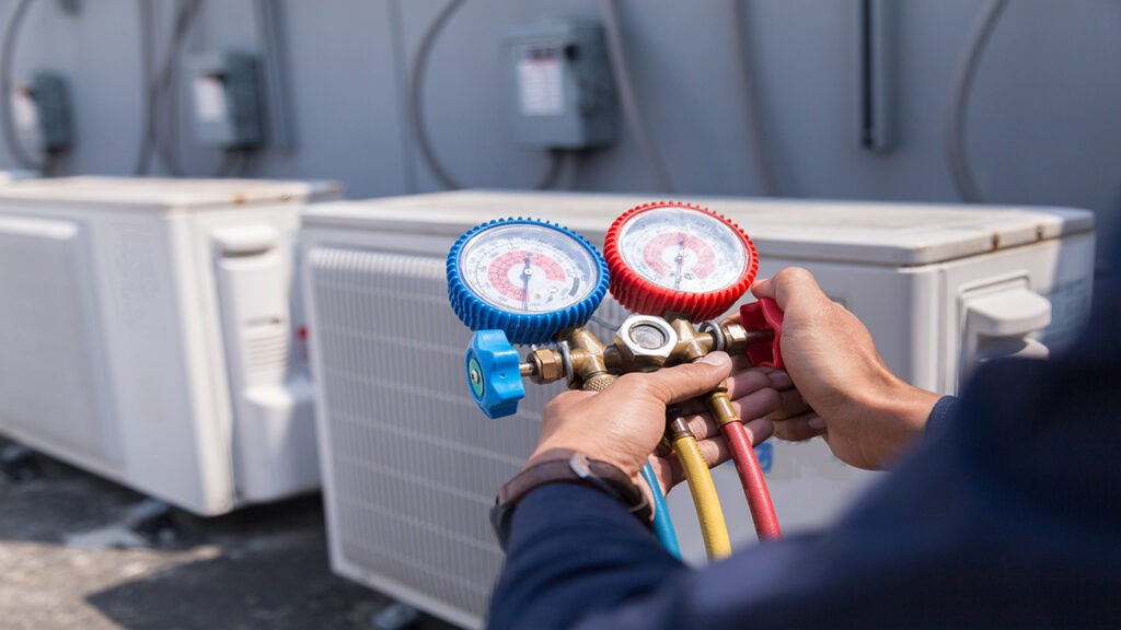 A person holding two gauges in front of an air conditioner.