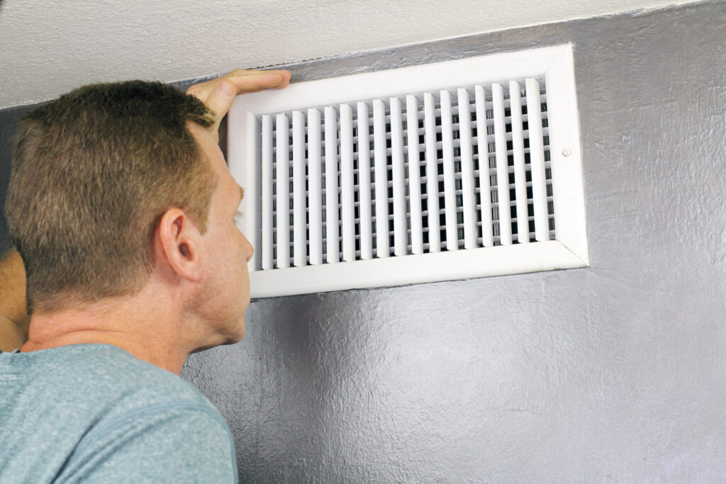 A man looking at an air vent with his hand on it.